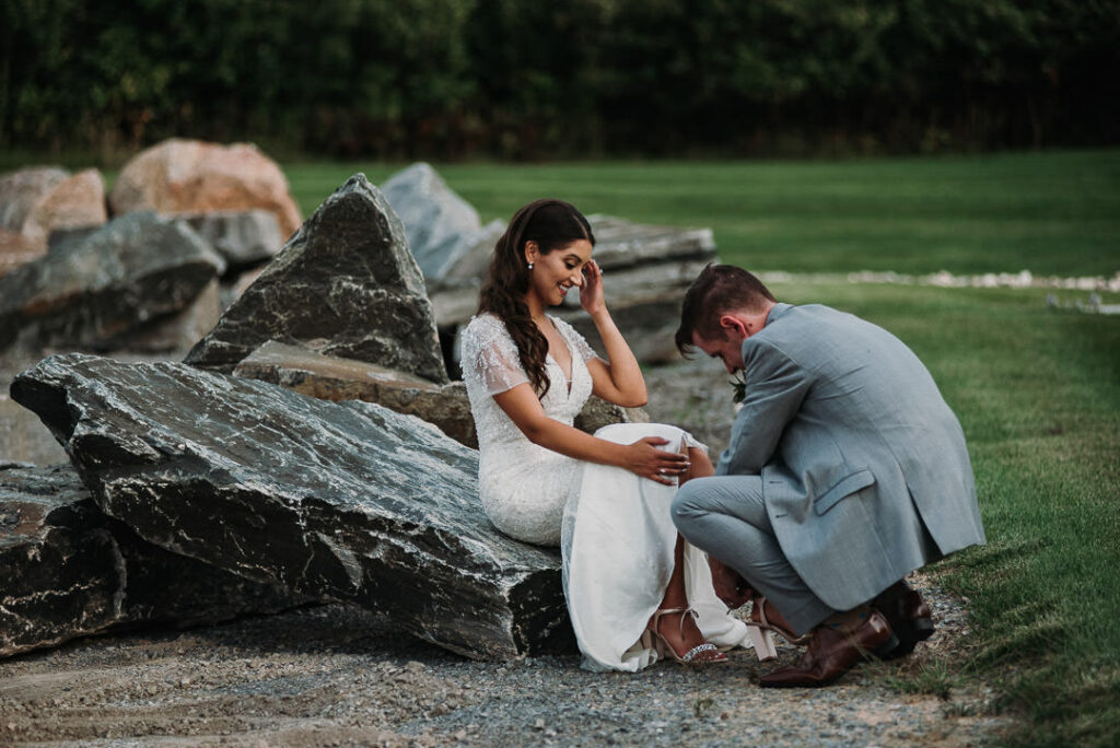 groom tying bride's shoes on grounds of aquatopia during their wedding