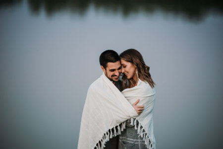 couple hugging under blanket in front of pond