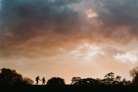 bride and groom silhouetted walking under big sky during arboretum engagement session