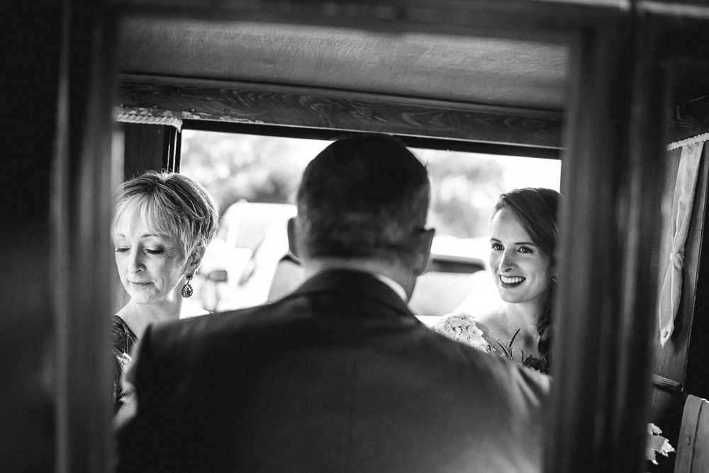 bride riding in car with father and mother to ceremony space