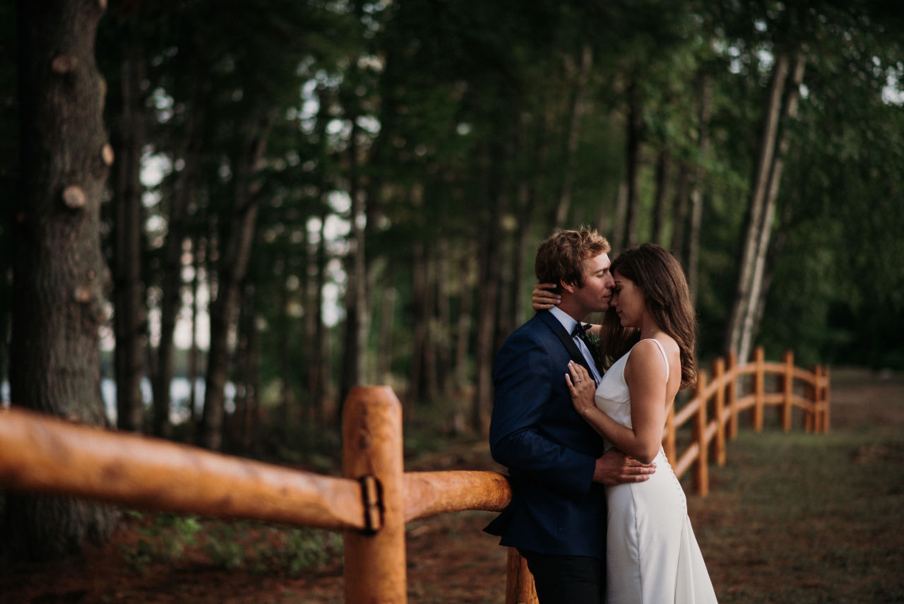 bride and groom holding each other next to log fence