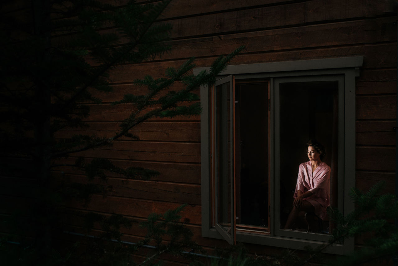 portrait of bride through window as she gets ready inside the lake house at wilderness tours